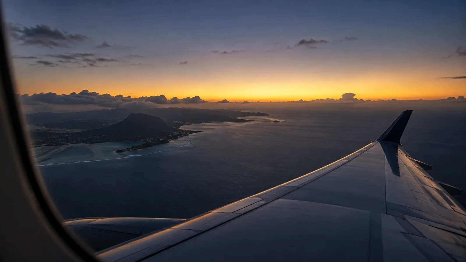 Vue d’illustration depuis un hublot au crépuscule : une aile sans marque au-dessus de l’océan, la côte d’une île qui s’éloigne